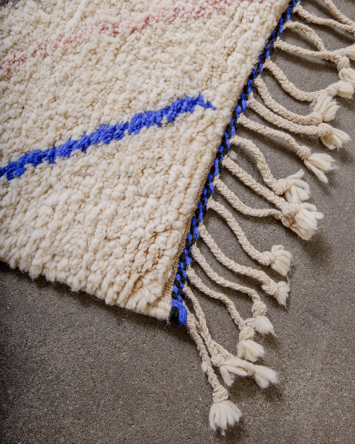 Corner of rug made of thick cream wool and natural wool tassels.